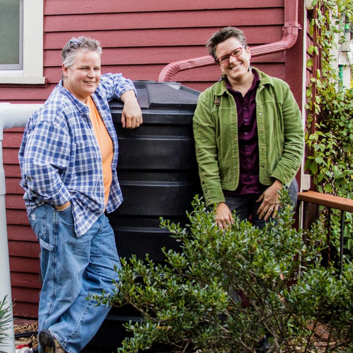 Two people standing next to a black cistern up against a red house